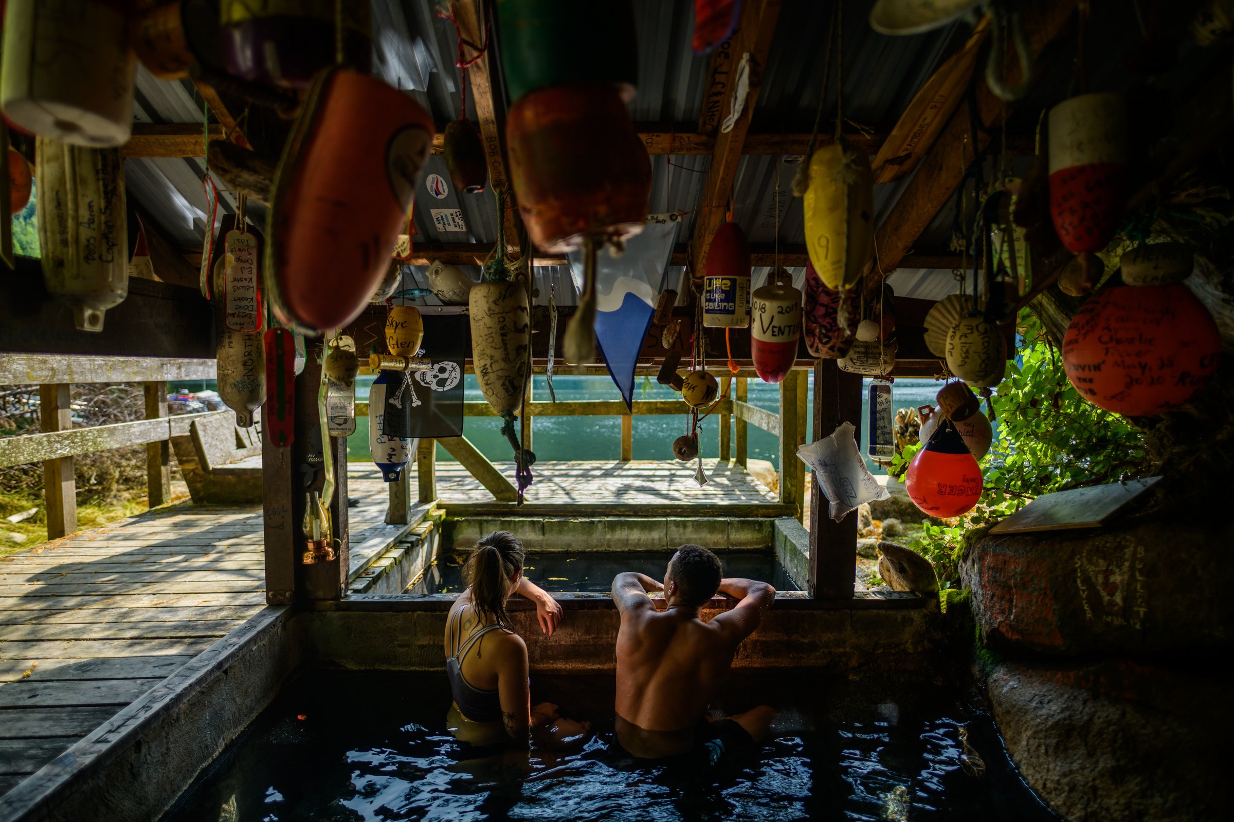 People soak in wooden hot springs tubs with fishing floats strung across the ceiling.