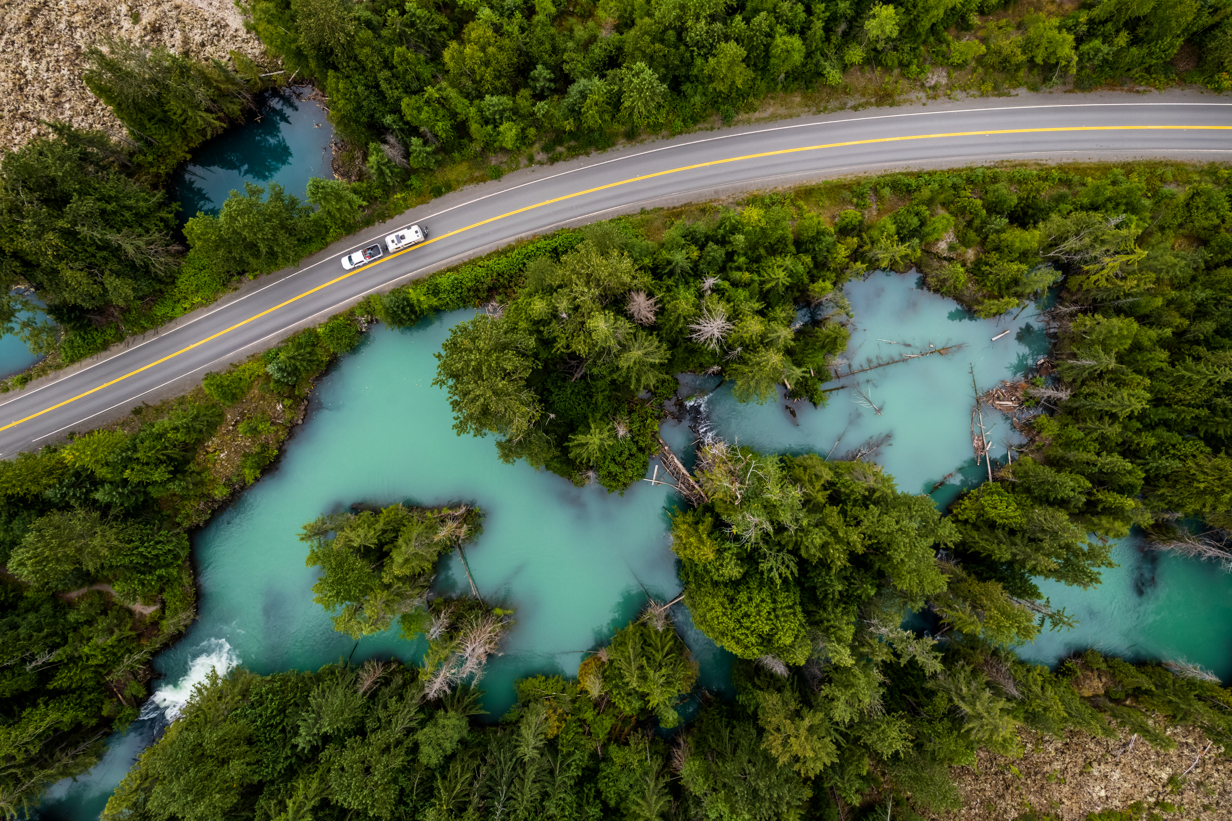 An aerial view of an RV driving through the Drowned Forest, a sea of turquoise water with forest growing into it.