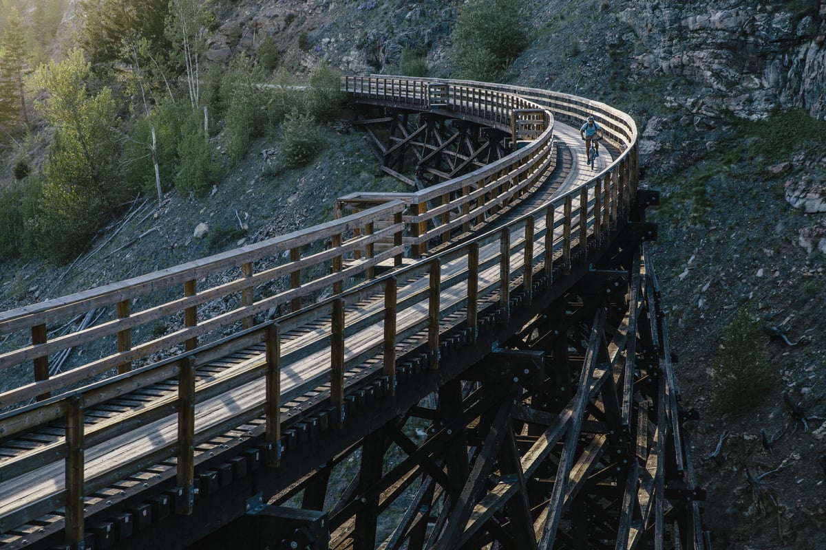 A wooden trestle bridge enters from the bottom left of the frame, and curves around and out the top left with a rocky bluff behind it