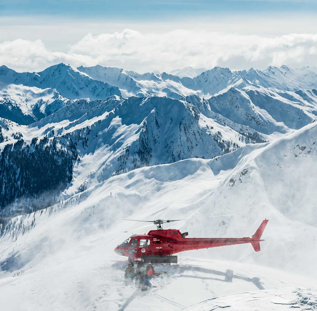 Group of heli-skiers being picked up by a helicopter near Mica Heli Skiing Lodge.