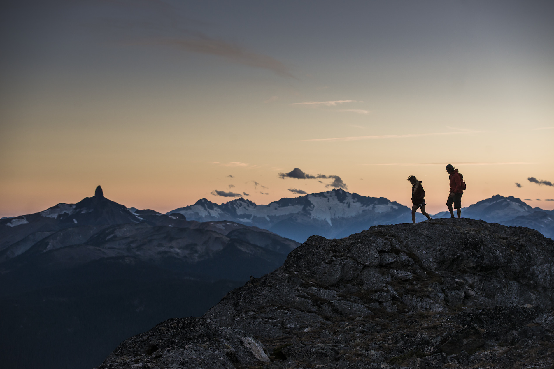 Two hikers stand against the sunset on the High Note trail. Black Tusk is seen in the distance.