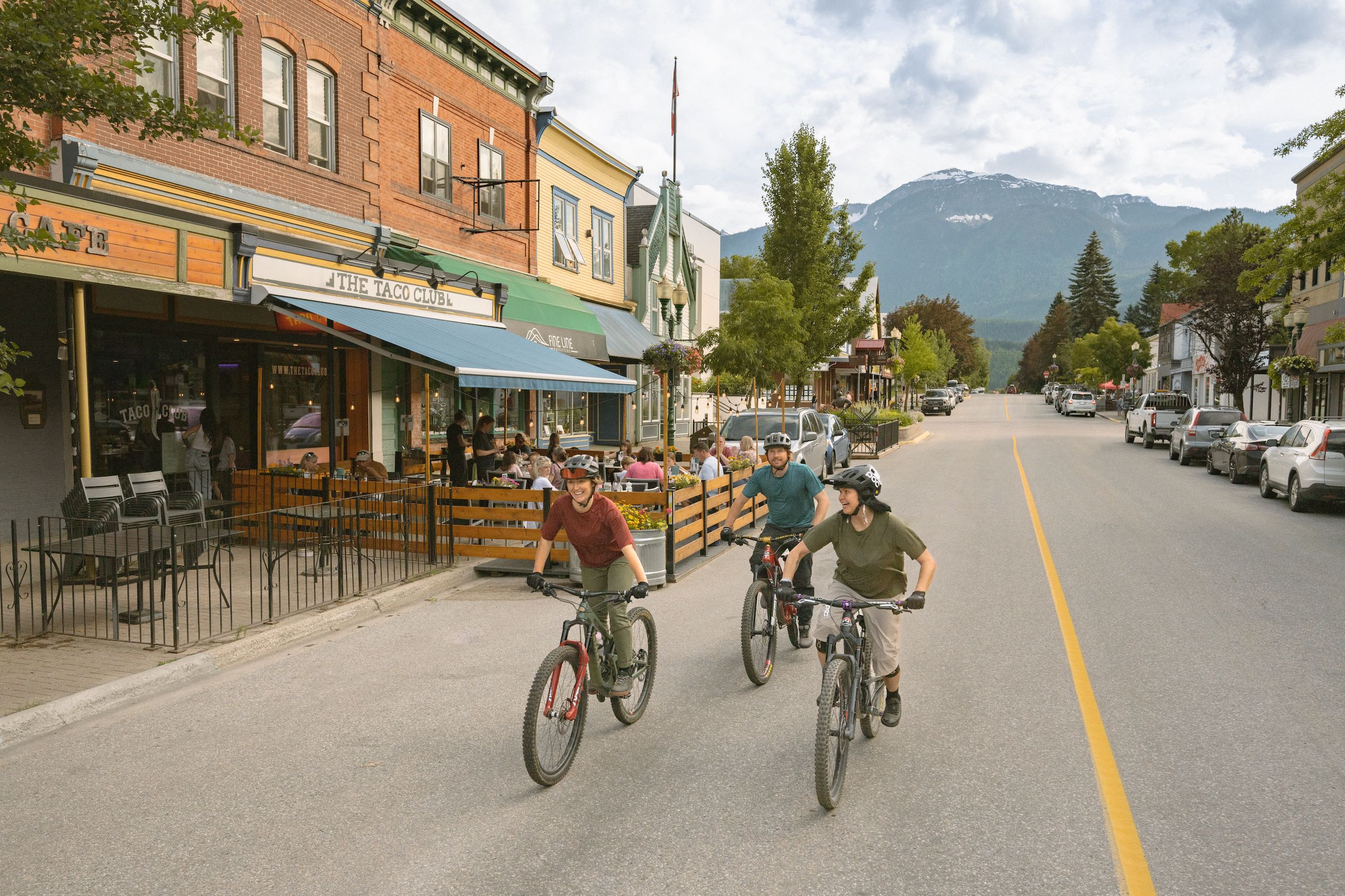 Three friends enjoy a bike ride in downtown Revelstoke as locals grab a bite to eat on The Taco Club patio.