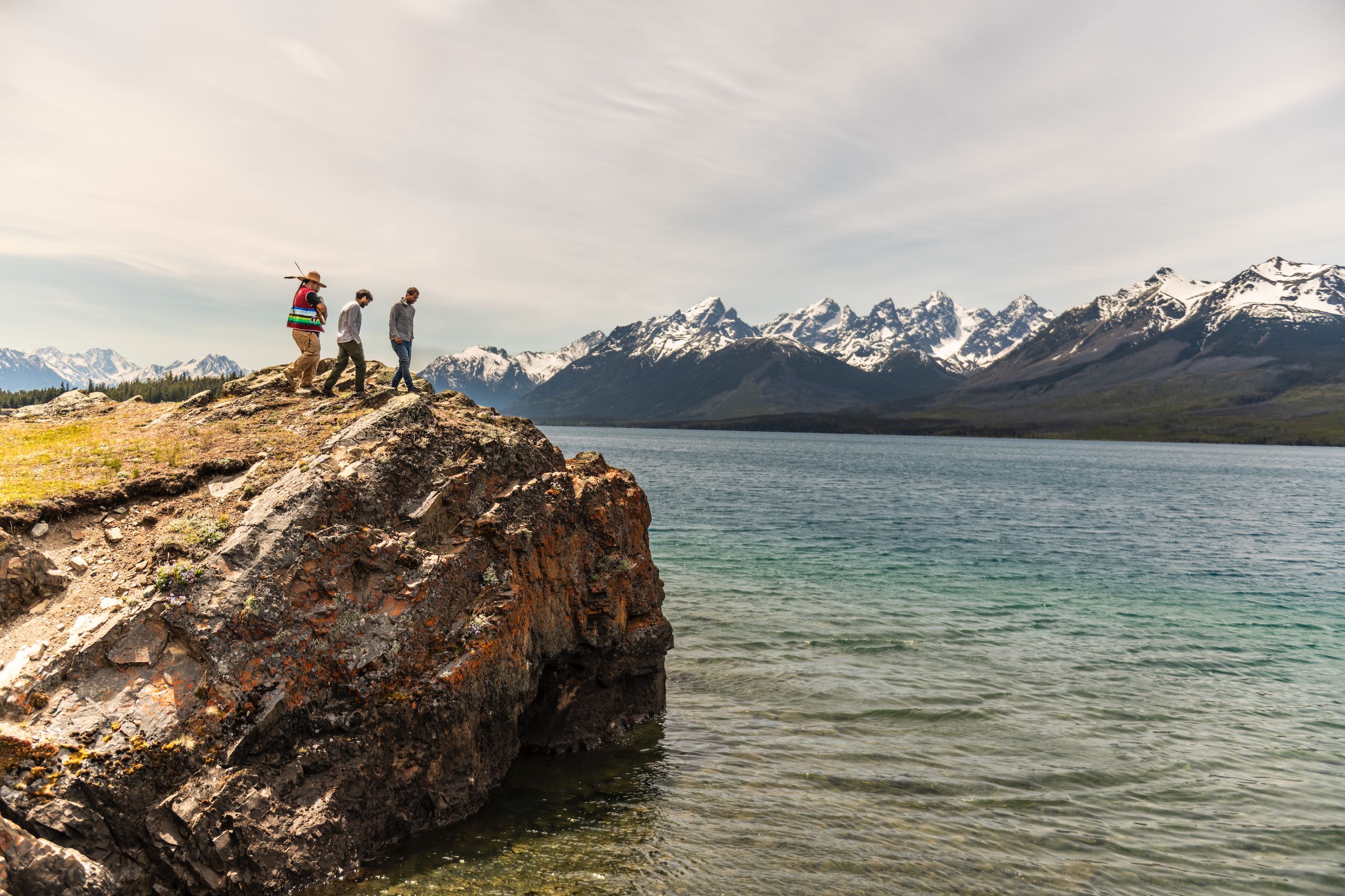 A father and son climbing a rock with their Indigenous guide while on a tour at Chilko Lake in Ts’ilʔos Provincial Park, with the scenic mountains in the background.