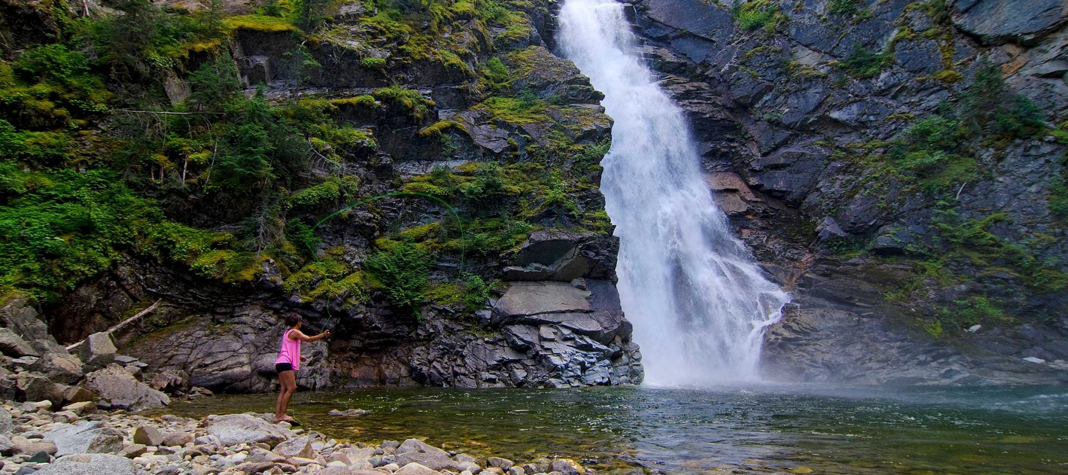 A waterfall and a person at the bottom looking up