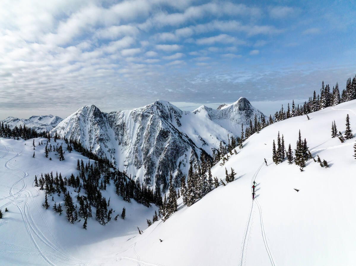 三个人背着滑雪装备，沿着被白雪覆盖的山坡向上行走。