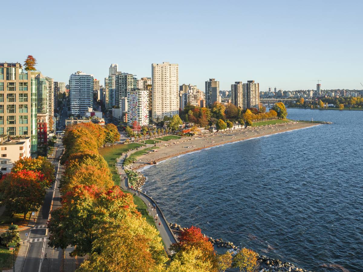 Aerial view over the ocean with a beach, trees, and highrise buildngs to the left.