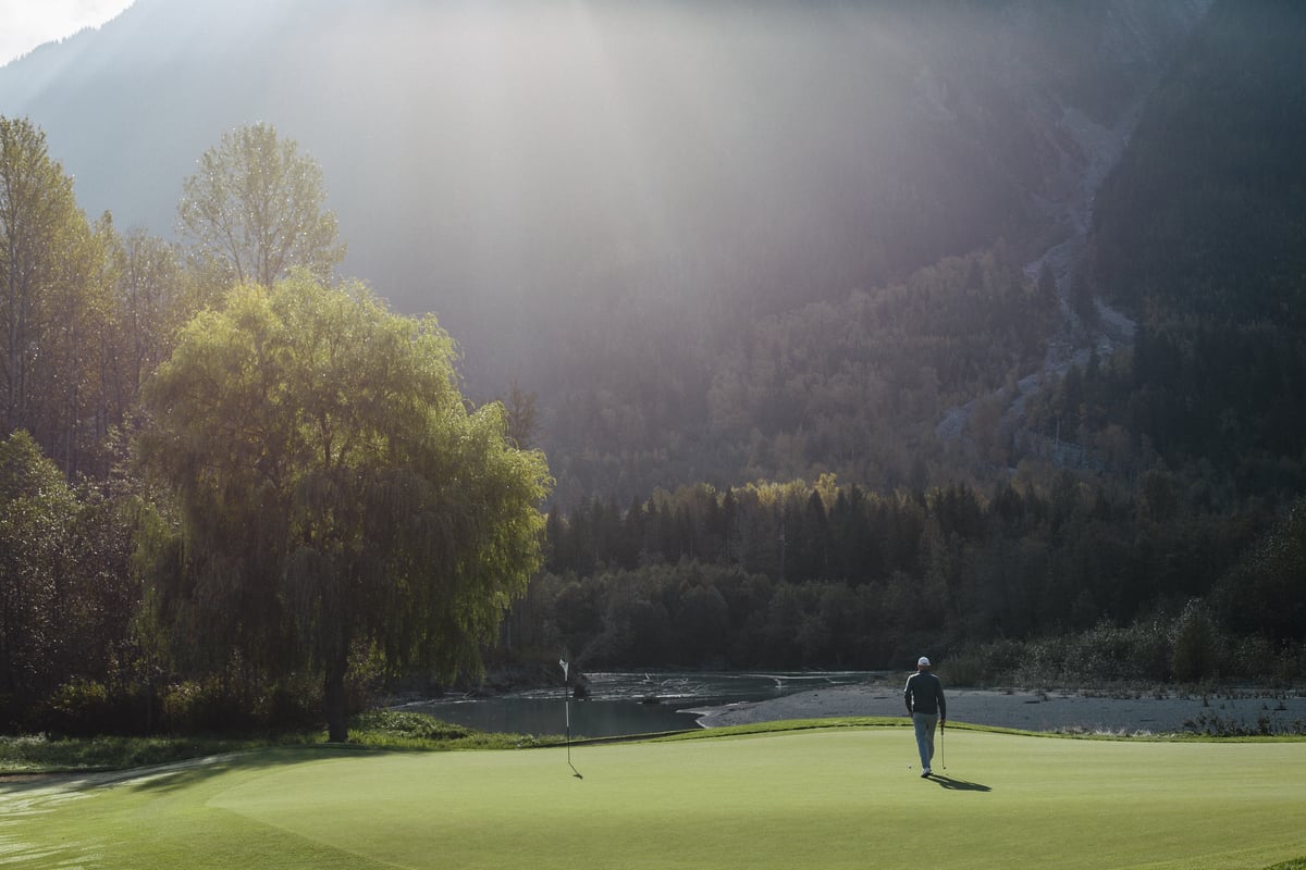 A golfer on the green looking up at the mountains at Big Sky Golf Club