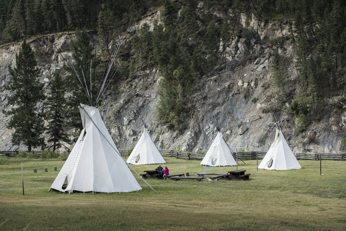 Four Teepees at Xatśūll Heritage Village on a grass field in front of a mountain.
