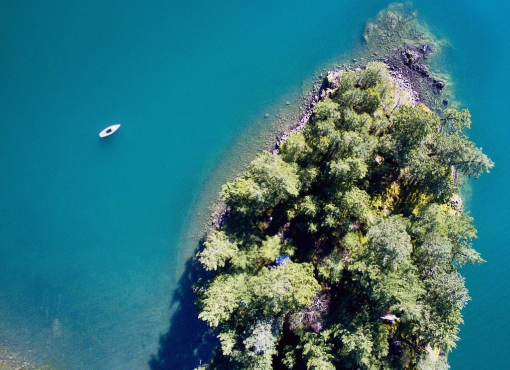 Aerial photo of a tree covered island surrounded by a bright blue lake with a kayak
